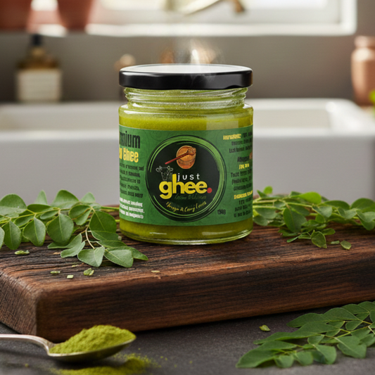 Moringa and Curry Leaves Ghee in a glass jar on a wooden surface with fresh leaves around it, promoting healthy digestion.